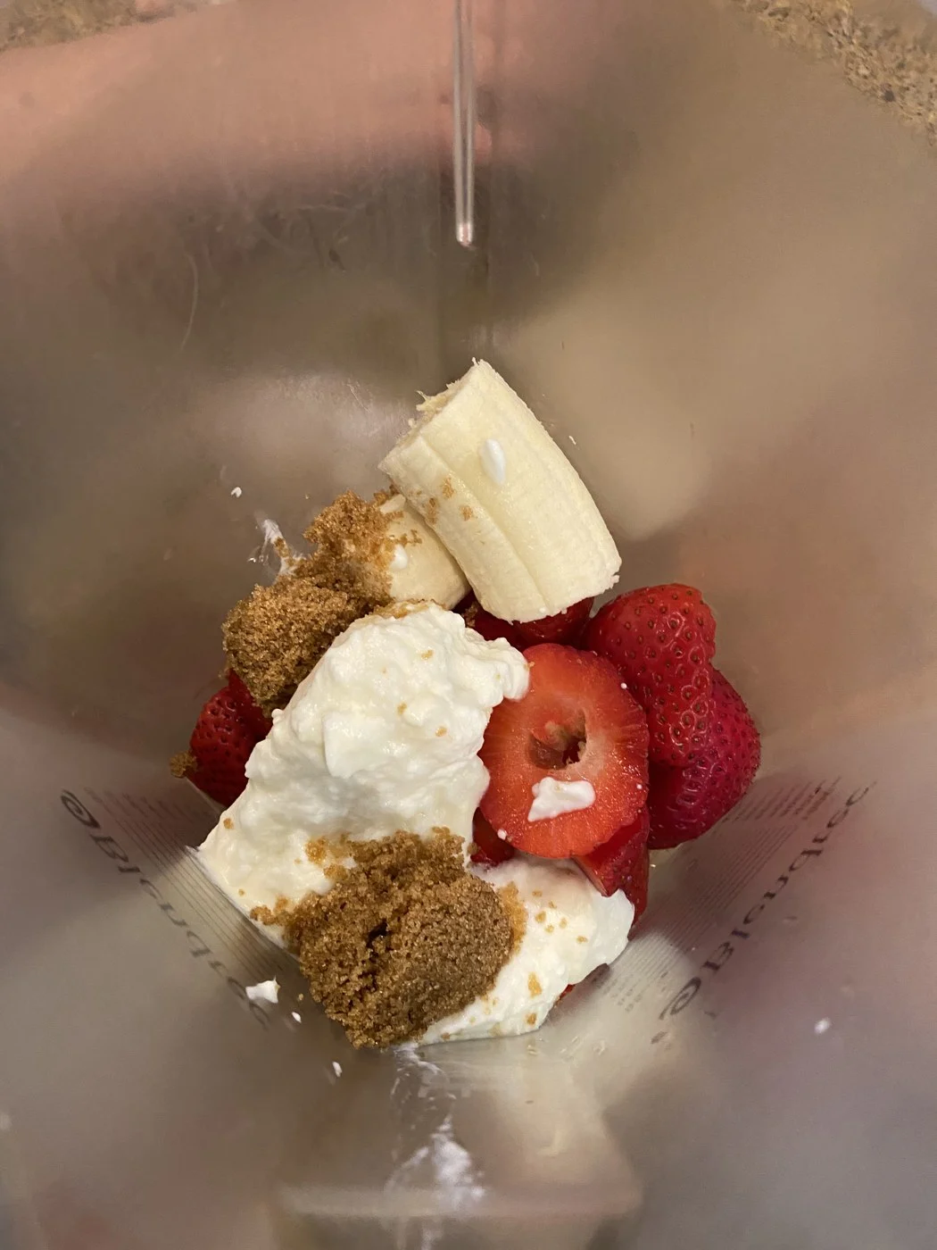 Looking into a blender jar containing strawberries, banana, a white mixture and brown granules.