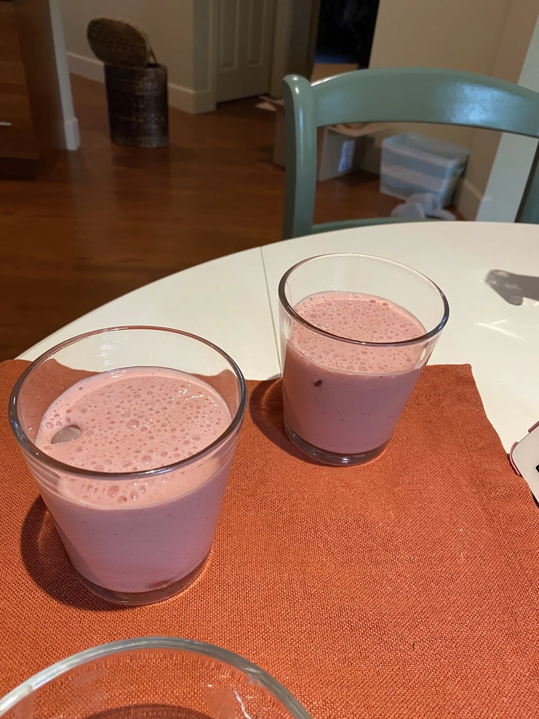 Two glasses of pink drink on an orange table mat.