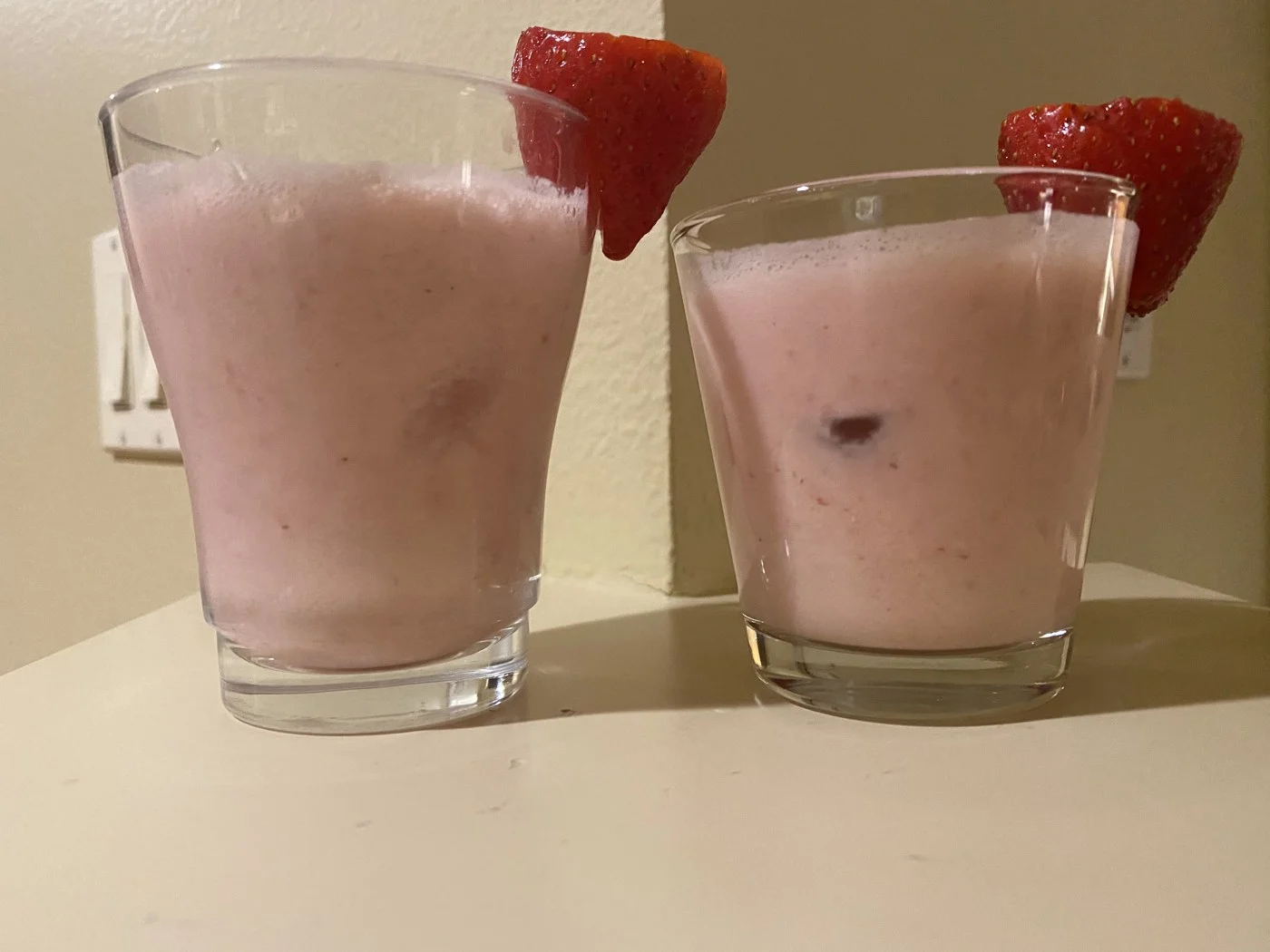 Two pale pink drinks garnished with strawberry halves.