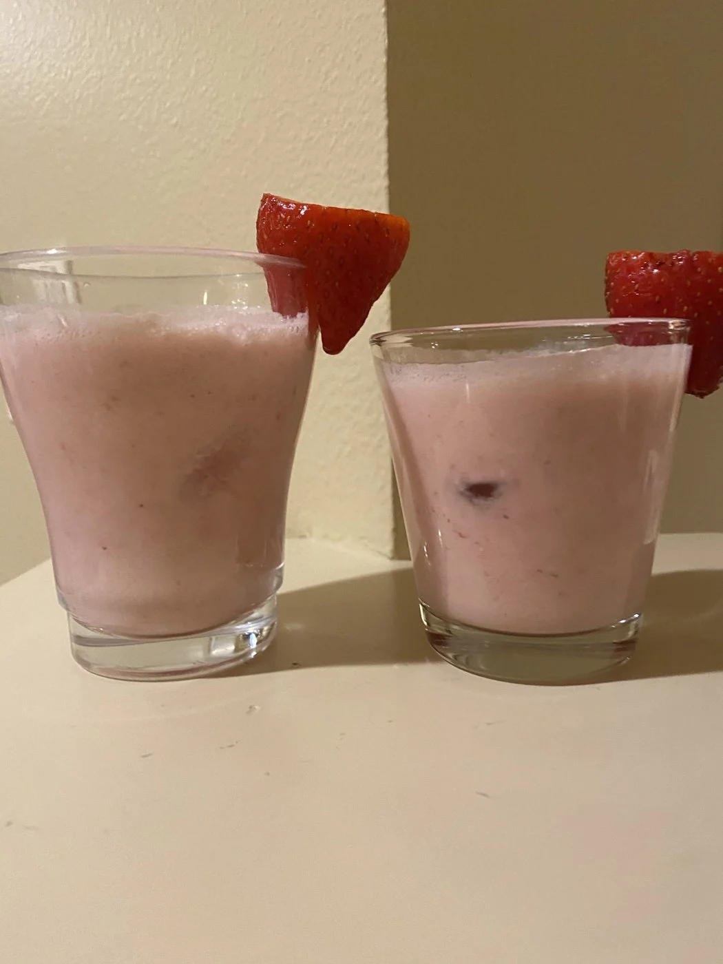 A tall and a short glass of pink drink with strawberries on the rims.