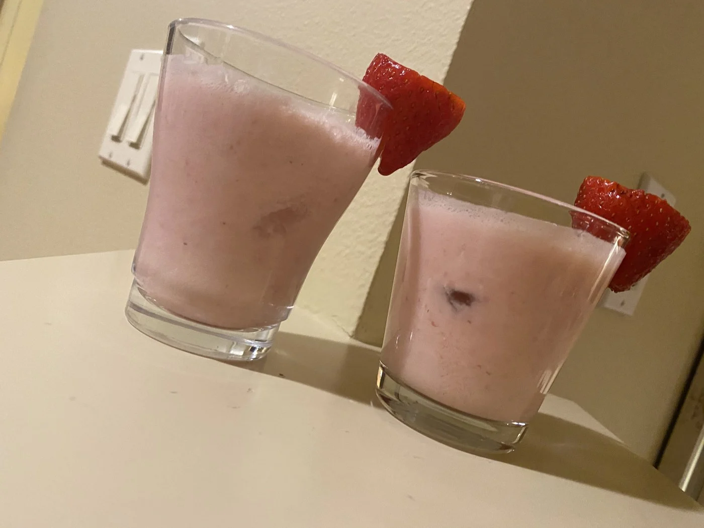 Two pink drinks photographed diagonally across a white table.