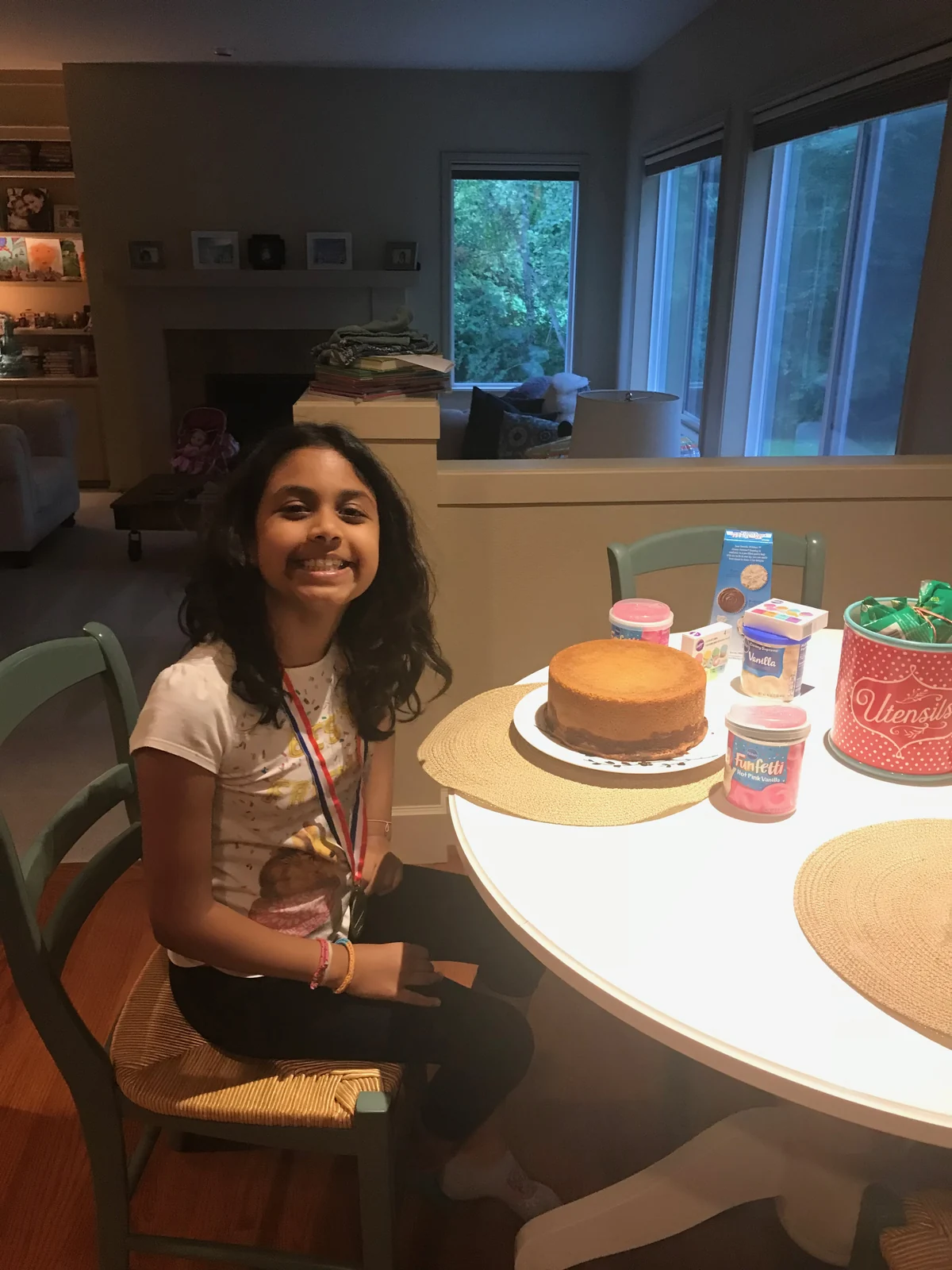Person beside unfrosted round cake, hot-pink frosting tubs and familiar decorating table.
