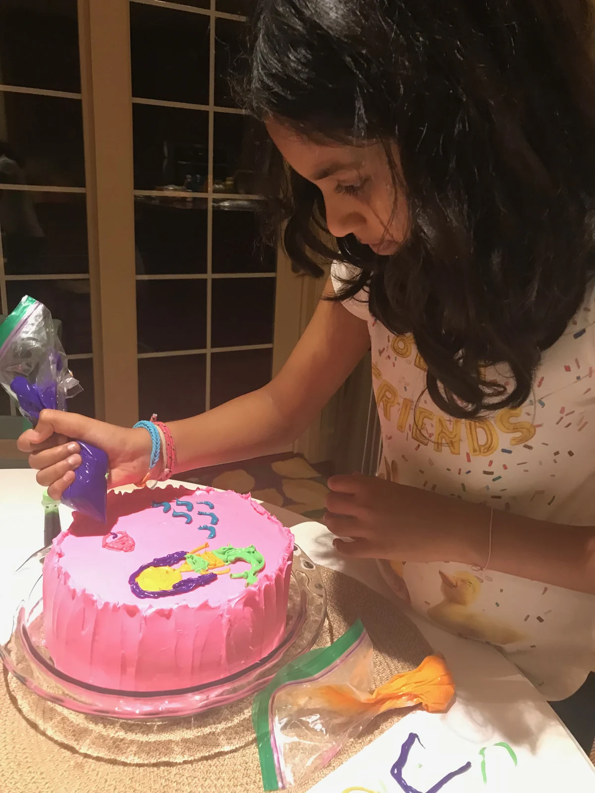 Piping on a pink-frosted round birthday cake at the same decorating table.