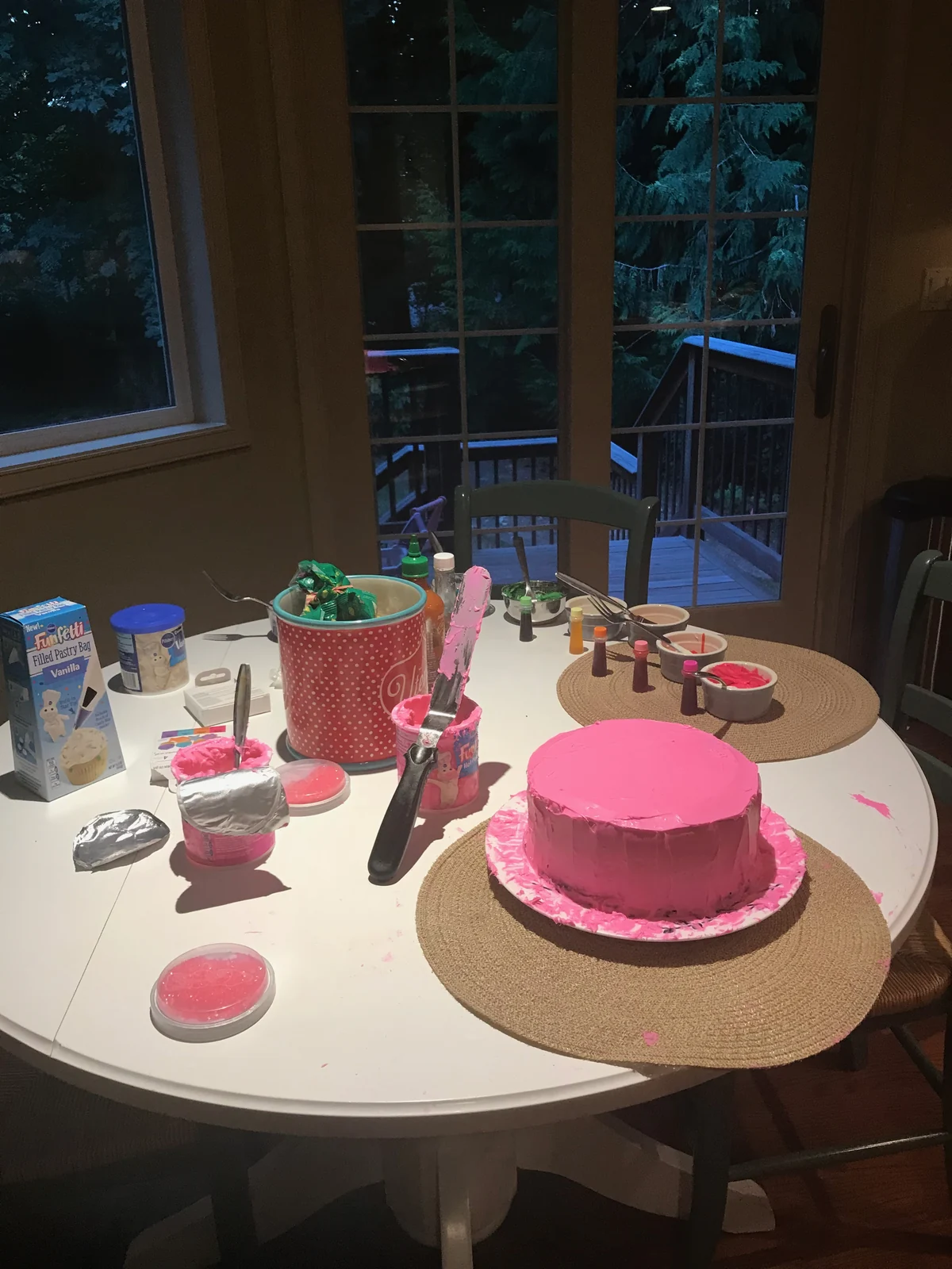 Plain pink-frosted round cake amid decorating supplies at the same table.
