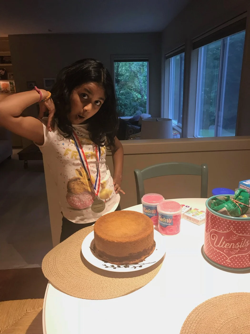 A baker posing beside a plain golden cake and pink frosting tubs.