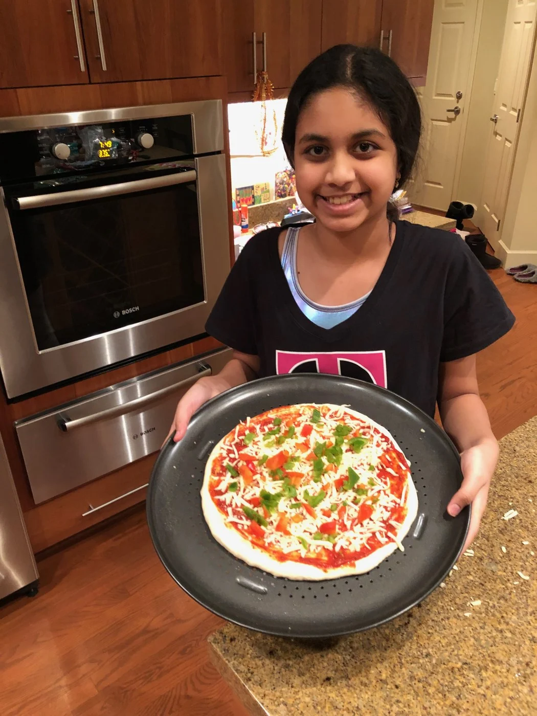 A baker holding a tray of topped pizza dough before baking.