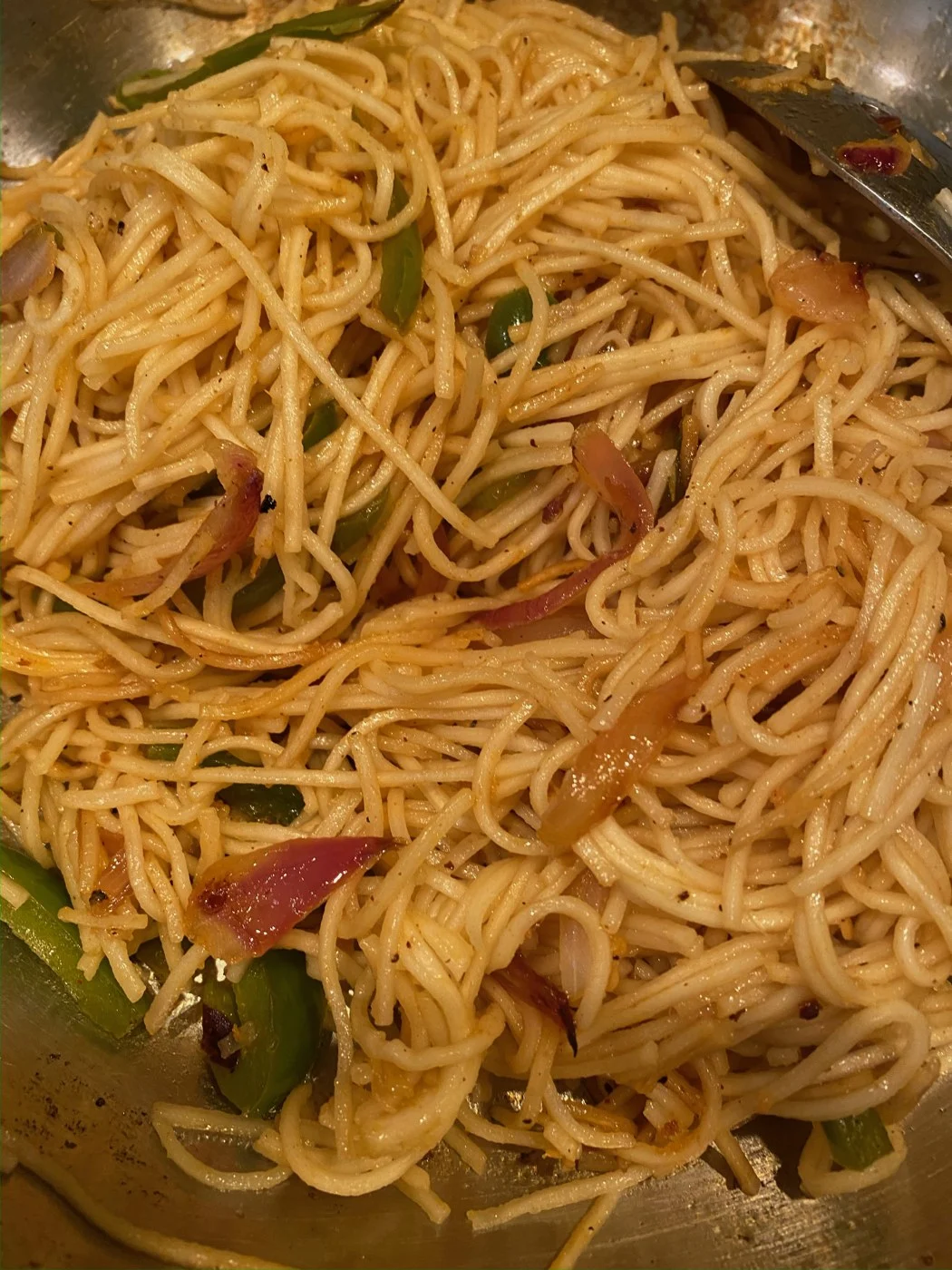 Long noodles tossed with sliced peppers and vegetables in a pan.